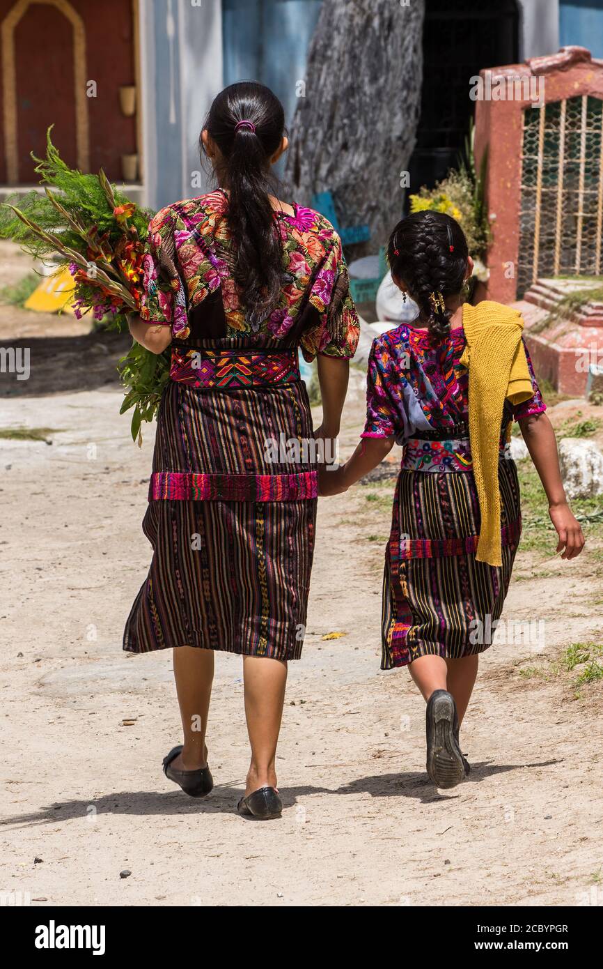 A Quiche Mayan mother and daughter in traditional dress bring flowers to place on a grave in the cemetery in Chichicastenango, Guatemala. Stock Photo