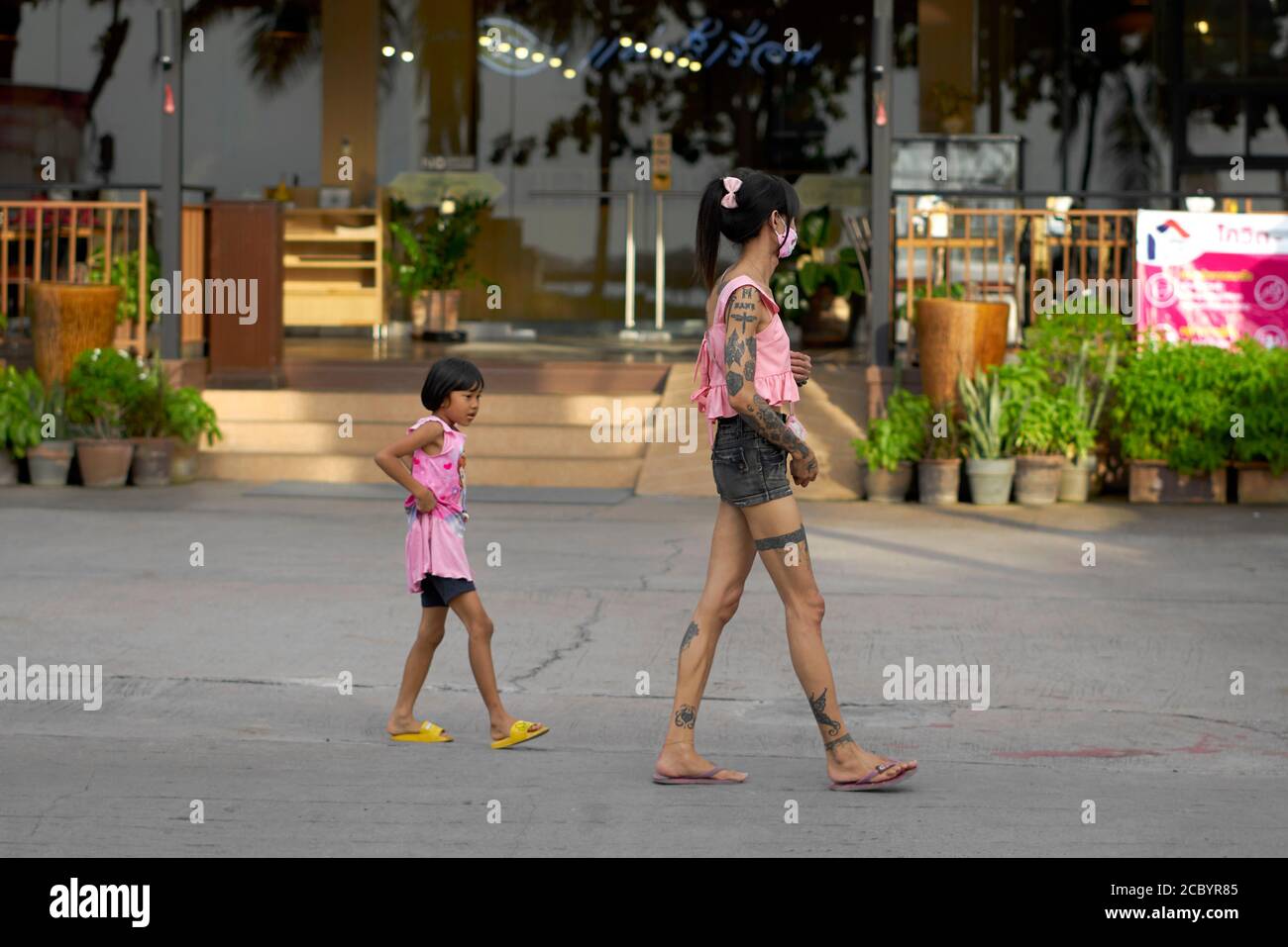 Funny child antics and Tattooed ladyboy. Thailand transsexual with extensive tattoos followed by young girl copying her. Stock Photo