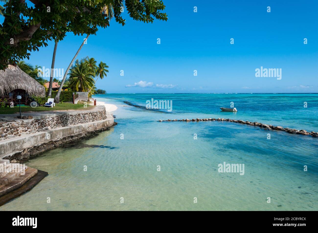 A seaside bungalows resort in Moorea. Paradisiac beach with an empty boat in the distance. Stock Photo