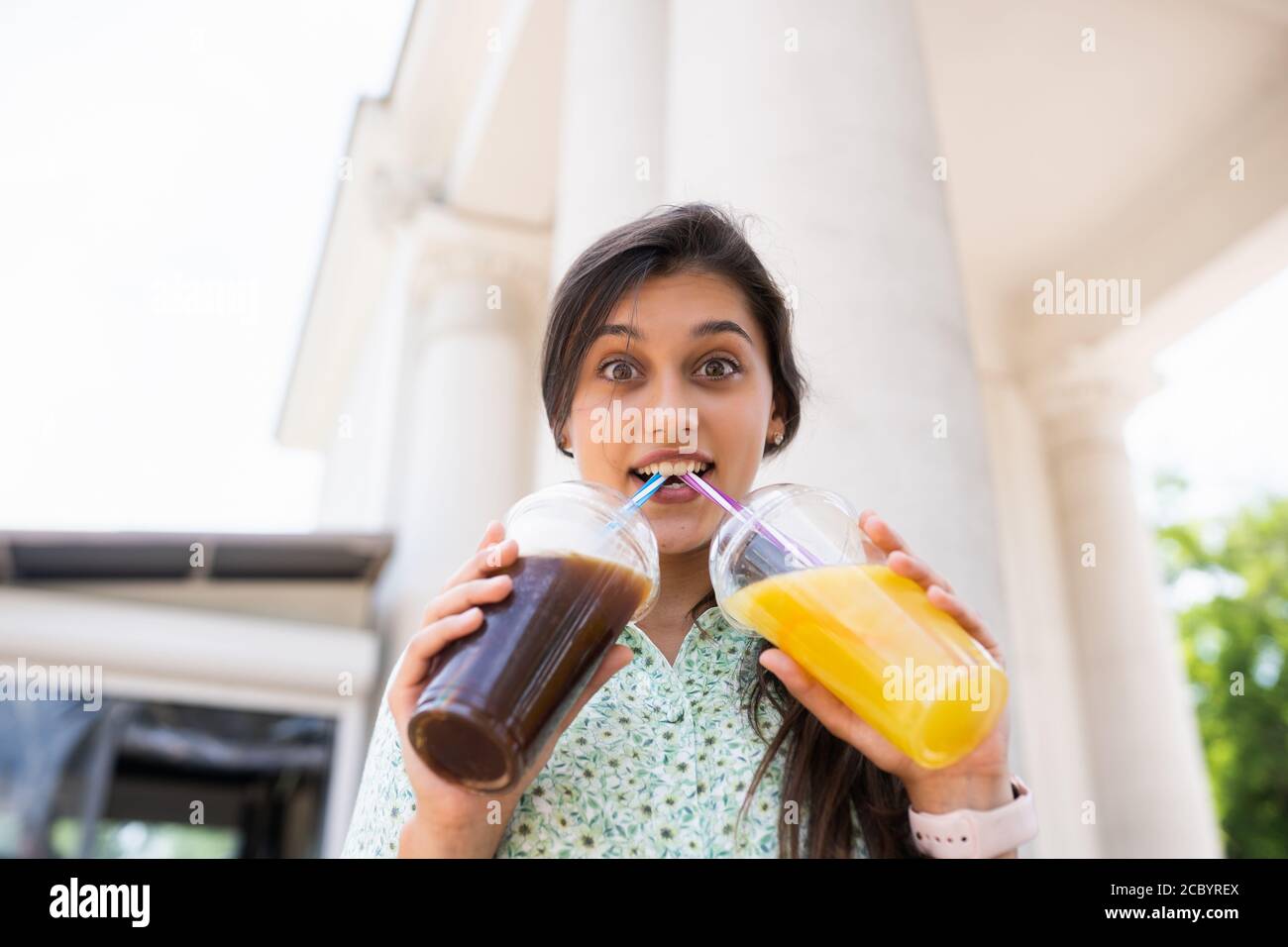 https://c8.alamy.com/comp/2CBYREX/young-woman-drinks-two-cocktails-with-ice-in-plastic-cups-with-straw-2CBYREX.jpg