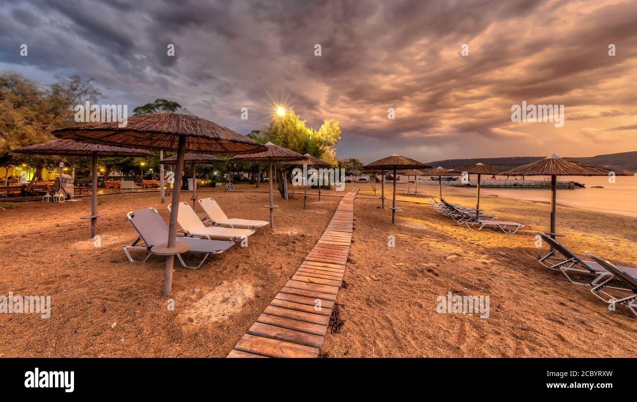 Reed parasols on empty peleponnese beach underclouded sky during colorful sunset Stock Photo