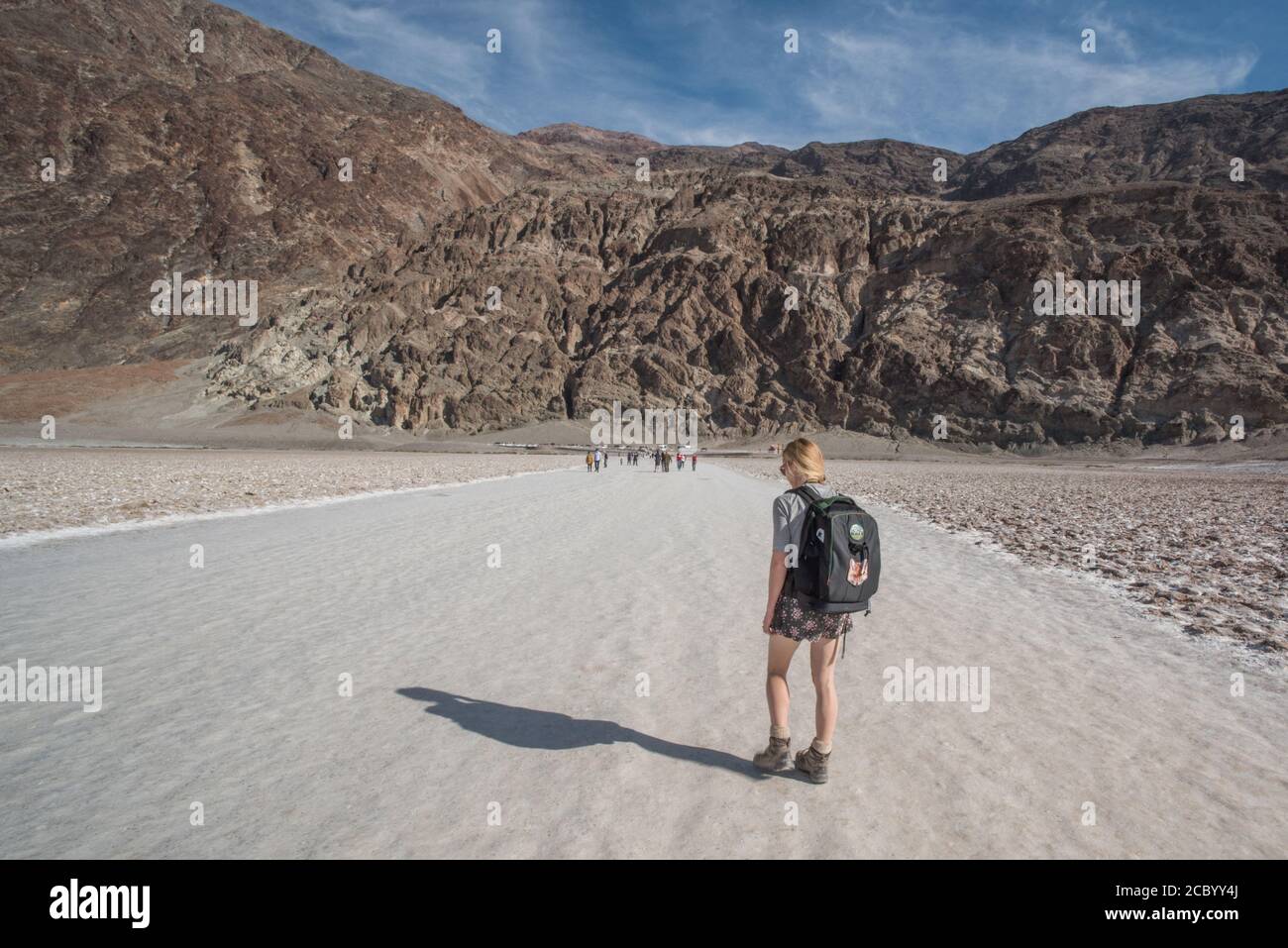 A hiker in badwater basin walking along the wide path back from the salt flat towards the mountains in Death Valley National Park. Stock Photo