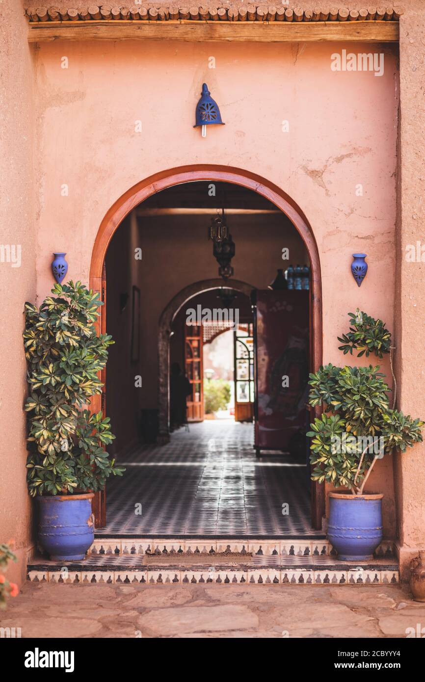Traditional moroccan style in architecture with red terracotta wall. Arch entrance, blue lanterns and clay flower pots with plants. Perspective inside. Stock Photo