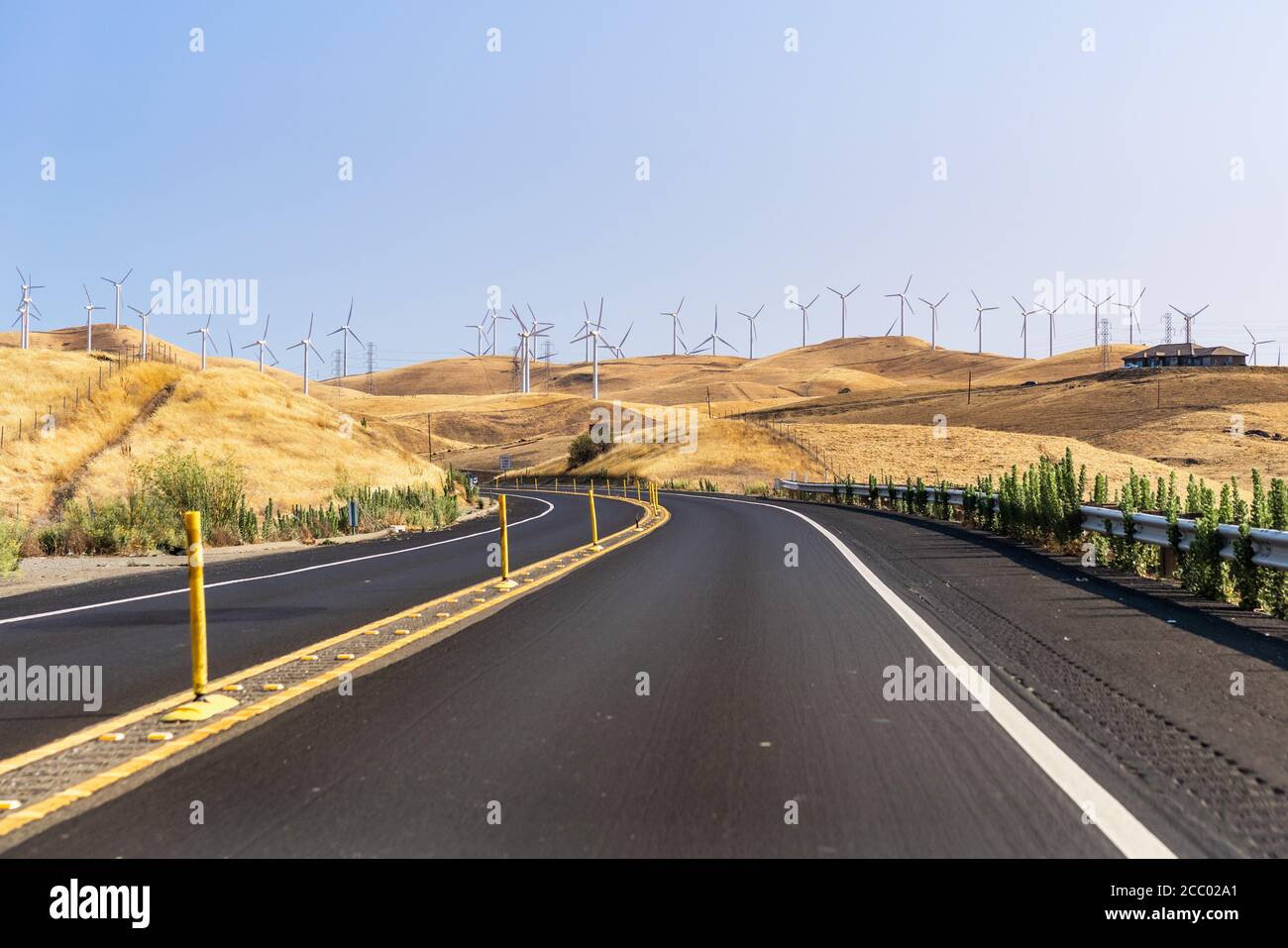 Highway crossing the hills and valleys of Alameda County close to Altamont Pass; Wind turbines visible on the golden hills; San Francisco Bay Area, Ca Stock Photo
