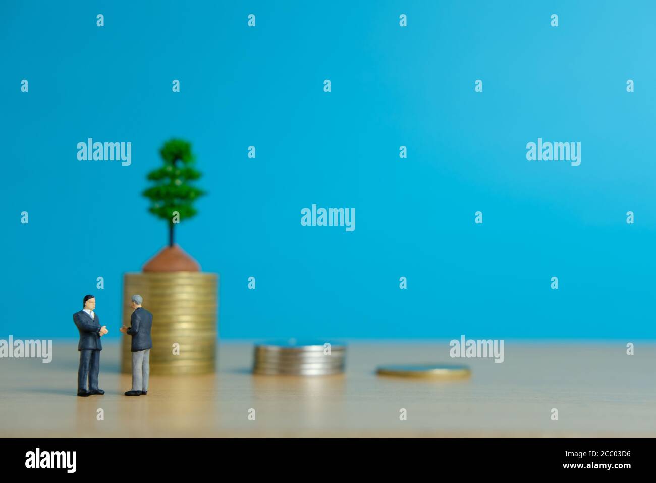Miniature business concept - two businessman make an handshake for partnership agreement handshake in front of coin stack Stock Photo
