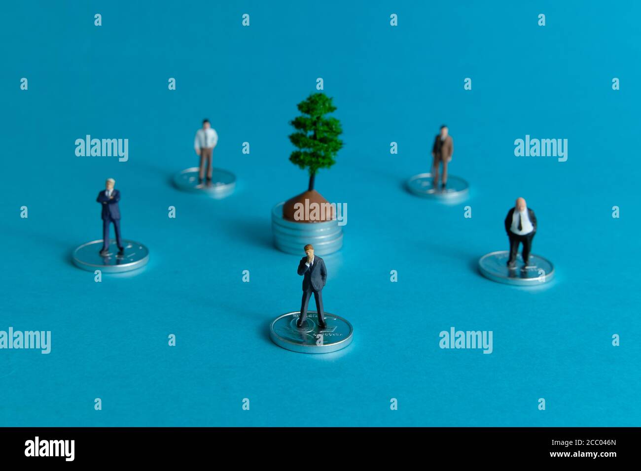 Miniature business concept group of businessmen stand around the coin