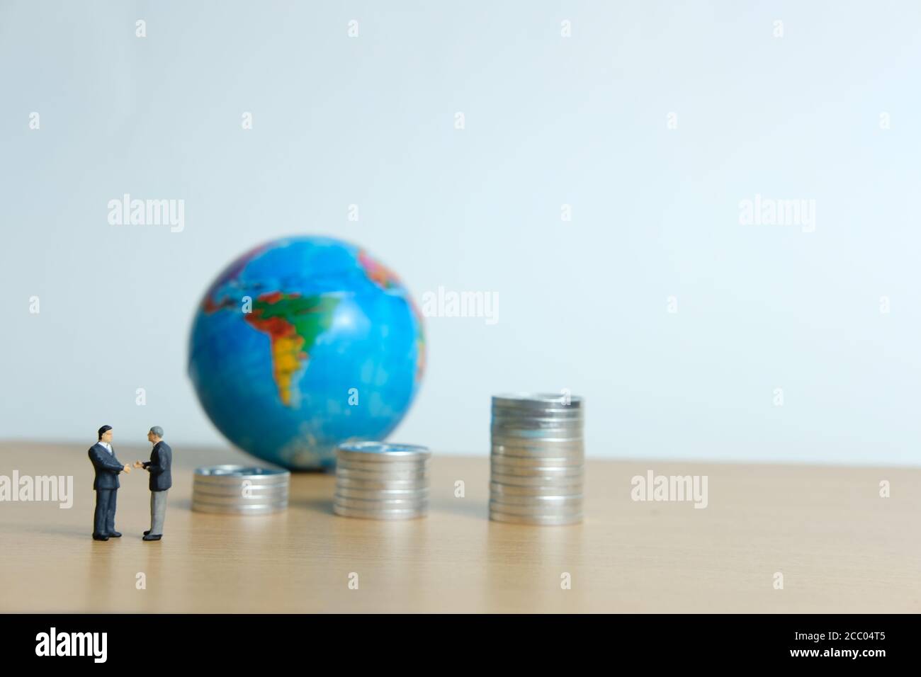 Miniature people business concept -Global trade partnership, with businessman, coin stack and globe Stock Photo