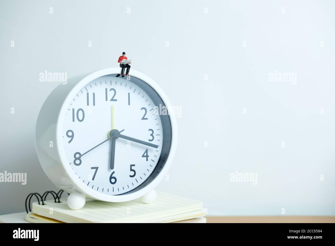 Miniature people for morning reading time concept - young man seating above clock reading a book Stock Photo