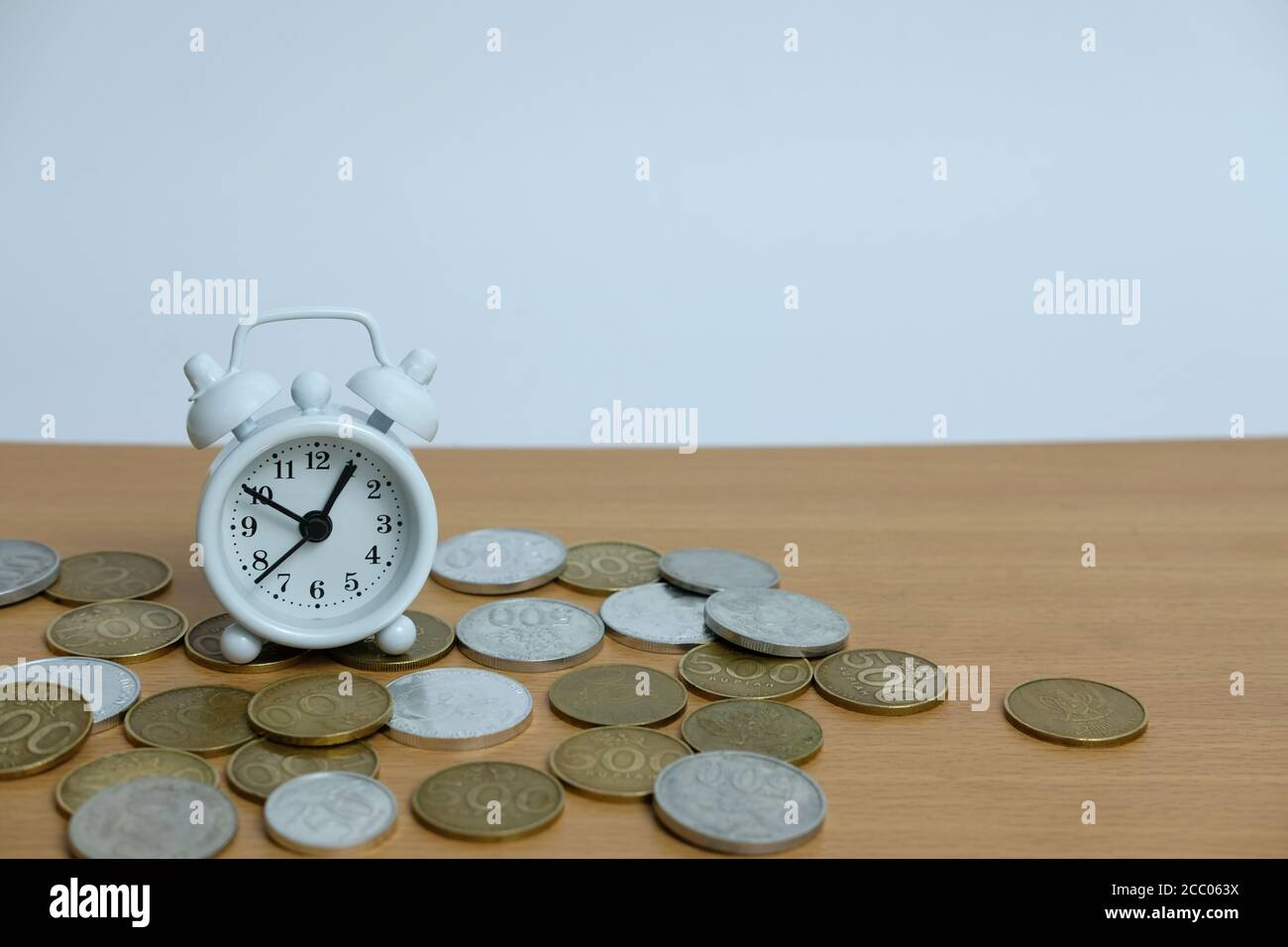 time is money concept - pile of money with white clock on a wooden table Stock Photo