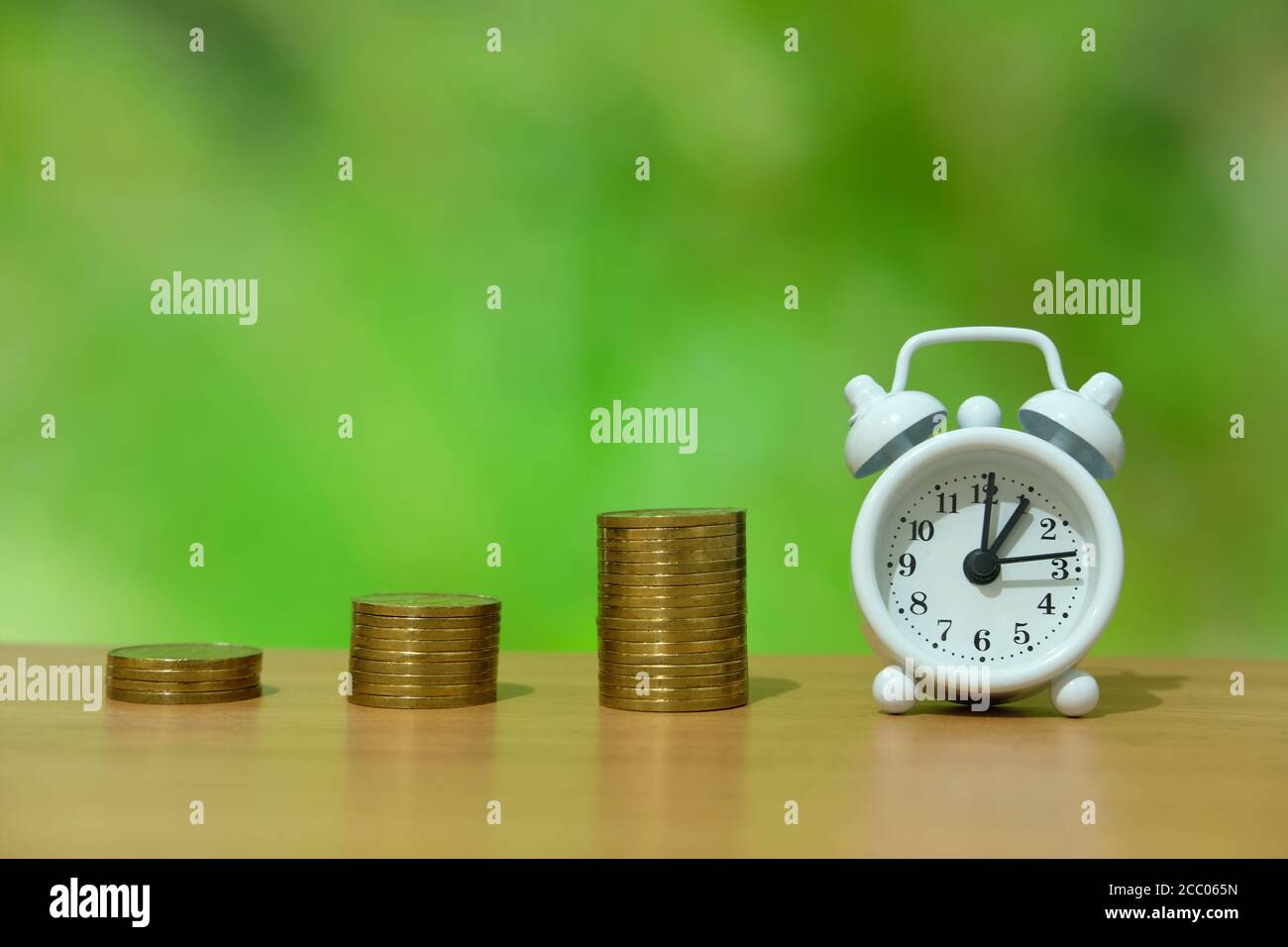 time is money concept - pile of money with white clock on a wooden table Stock Photo