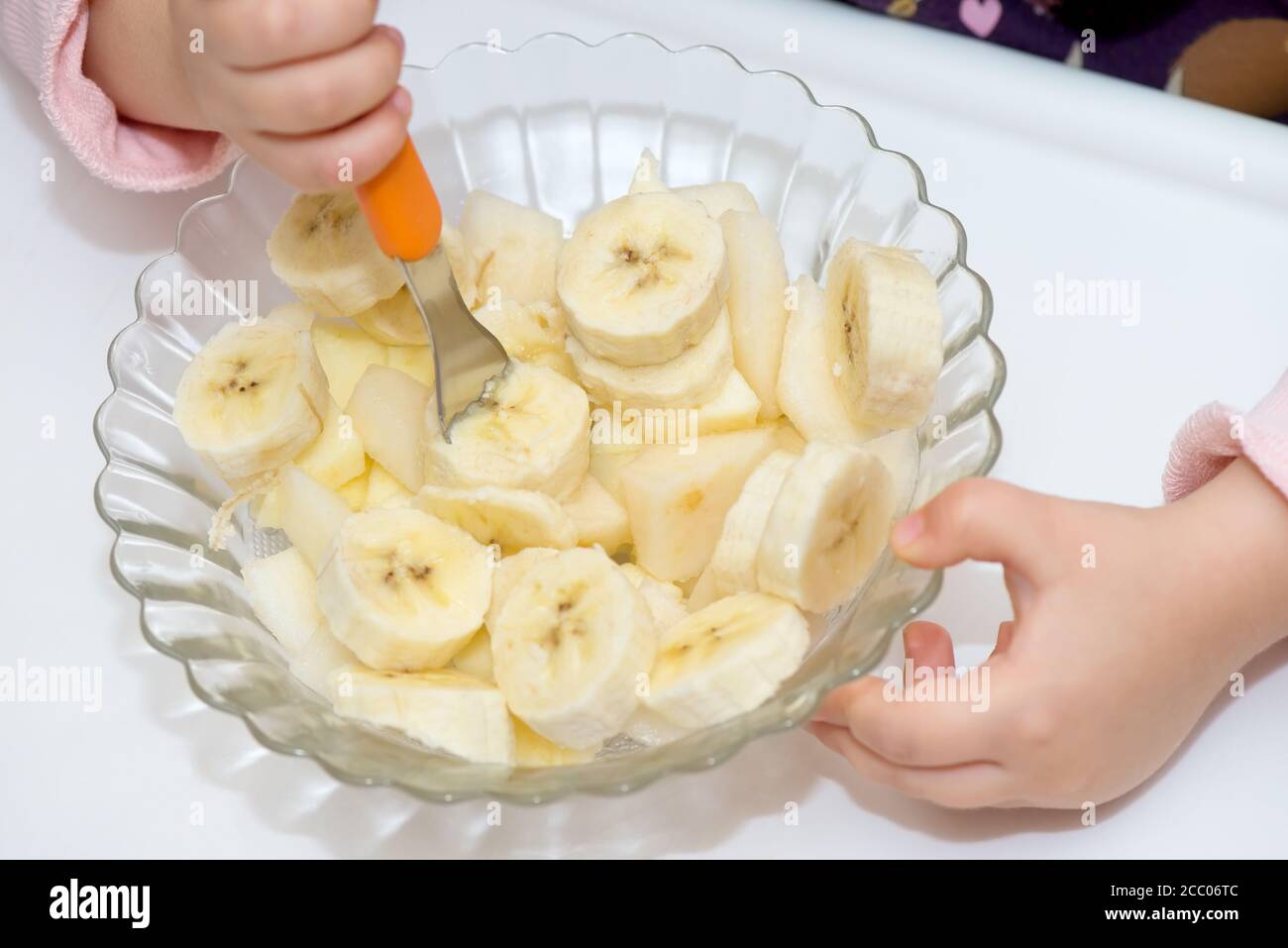 Detail of a glass bowl with banana slices and baby hands Stock Photo