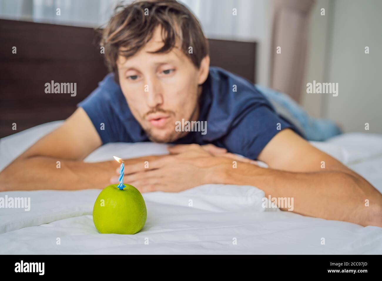 Quarantine birthday. Man with a smartphone and birthday cake-apple with candle. Stay home while quarantine. Online call. Video conference Stock Photo