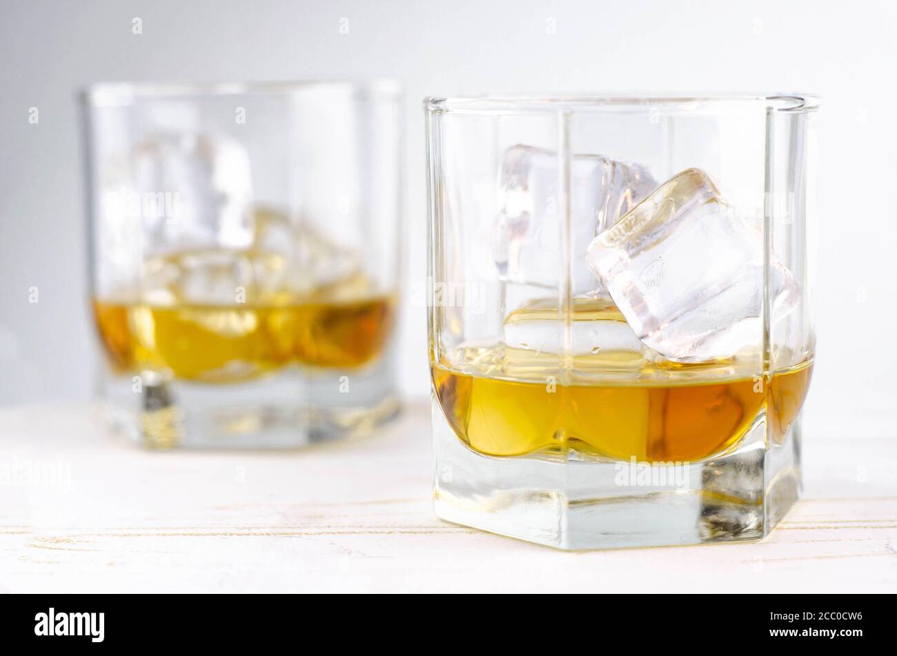 Two glasses of scotch whiskey with ice cubes, white background, wooden