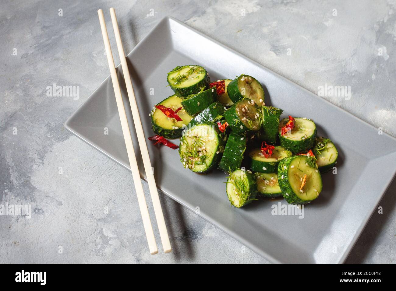 Asian beaten cucumber salad with chili and sesame seeds on a concrete background. Chinese food concept. Stock Photo