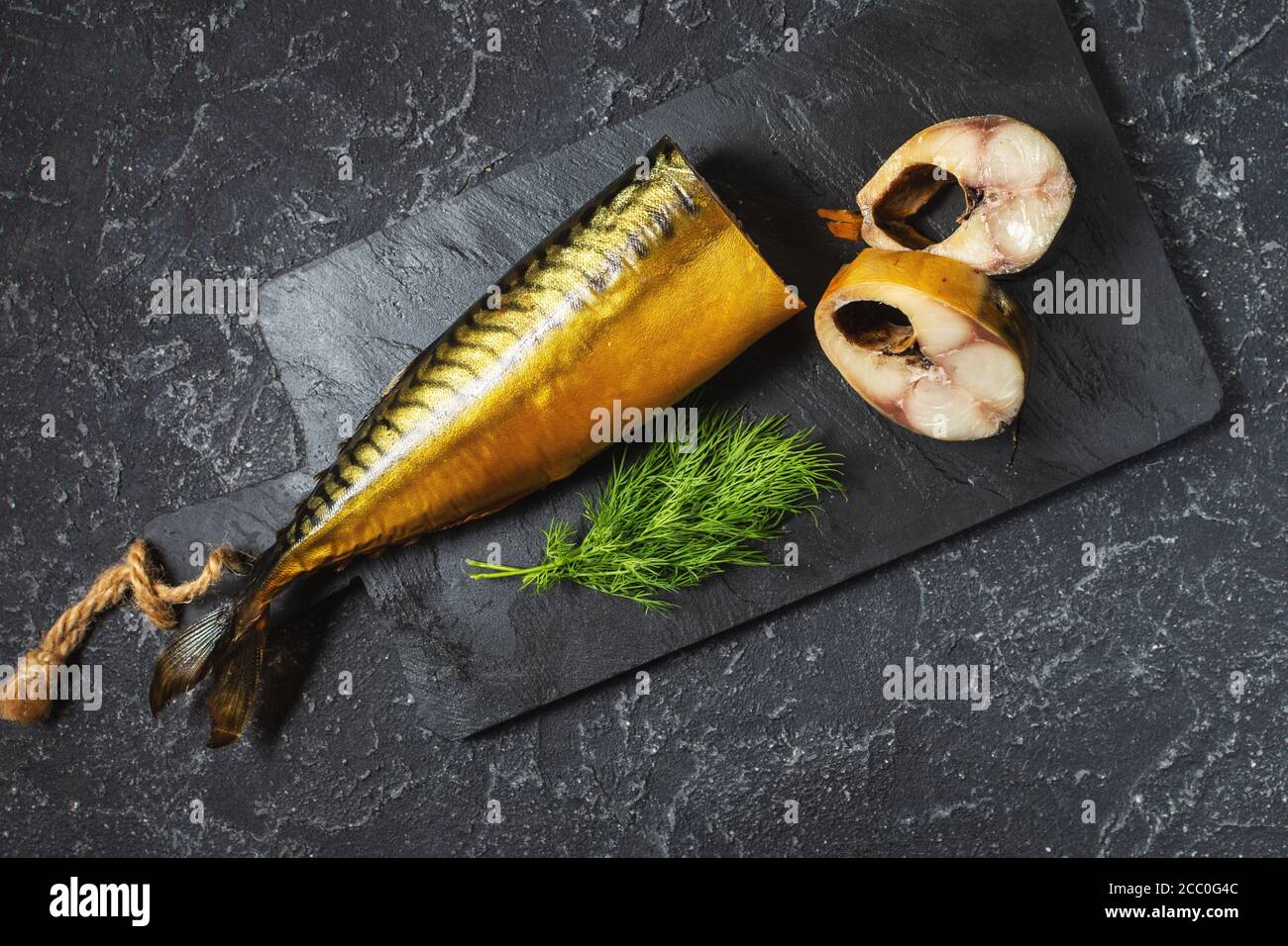 slices of smoked fish mackerel or scomber on black stone table. Top view Stock Photo