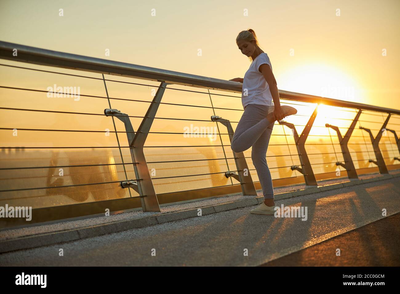Beautiful woman stretching legs on the bridge during sunrise Stock Photo
