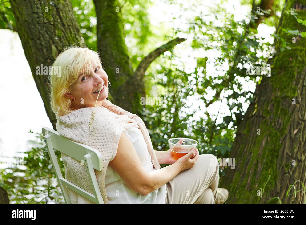 Old woman looking for relaxation in the garden in summer with a cup of tea Stock Photo