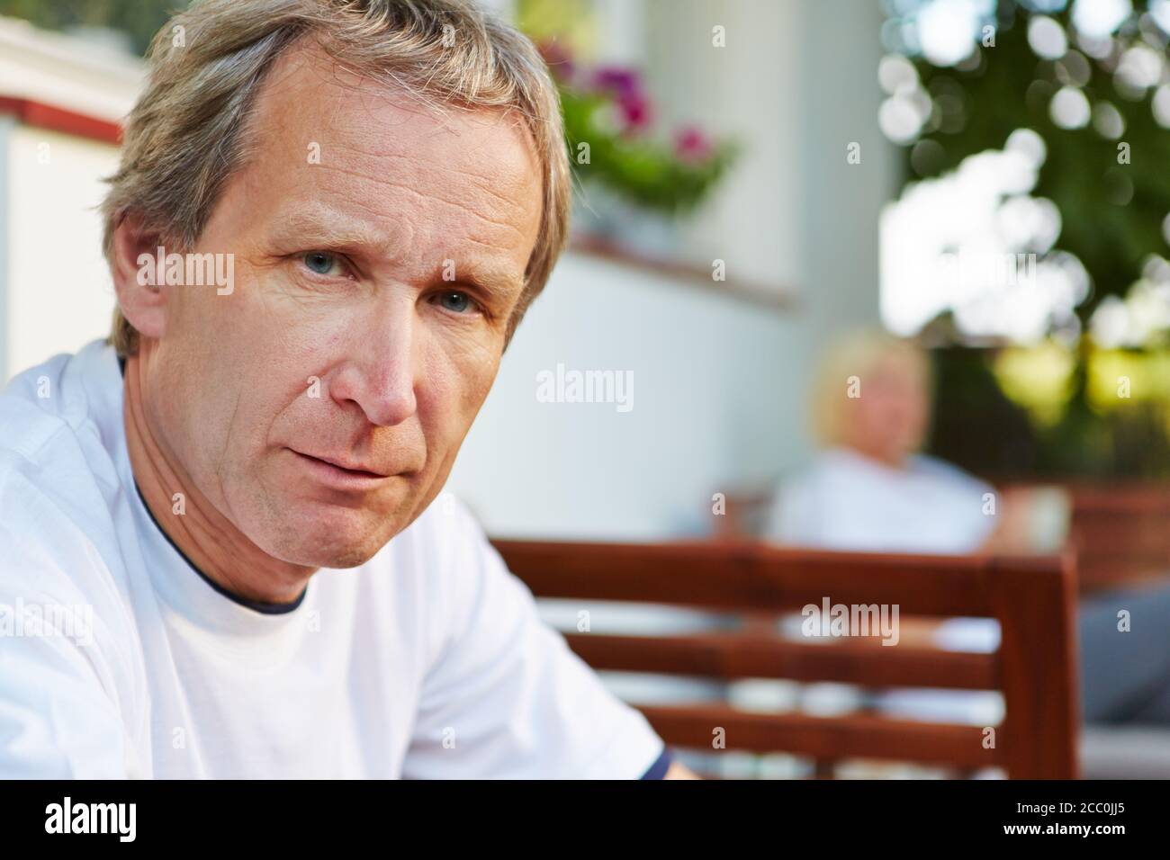 Old man sits in front of his house in summer and looks serious Stock Photo
