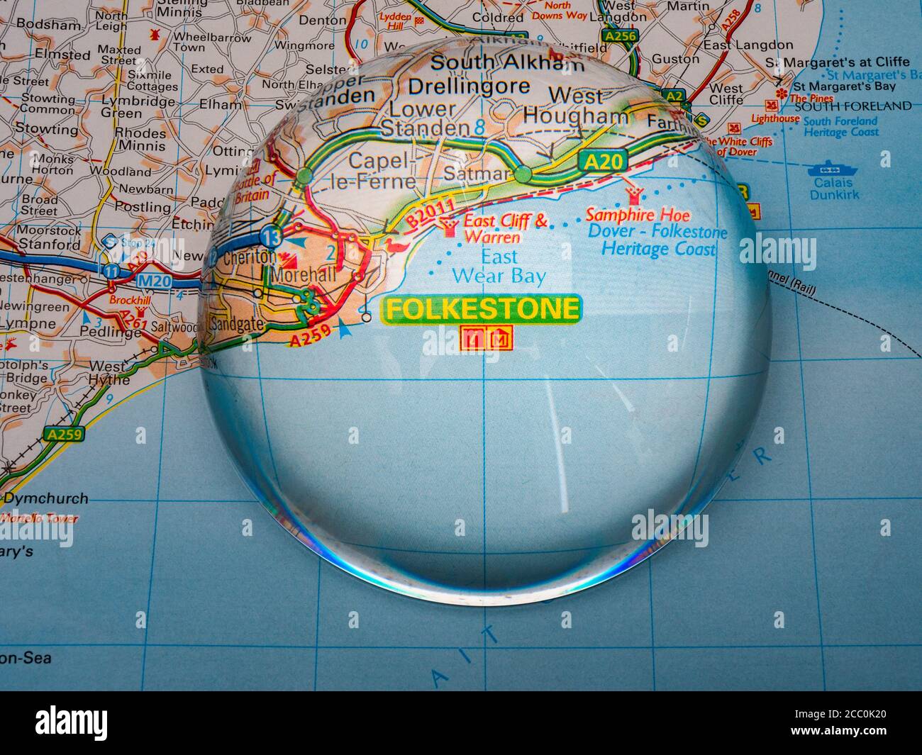 Closeup of a dome shaped magnifying glass over a page of a British road atlas map, with the Folkestone area of England enlarged for a closer view. Stock Photo
