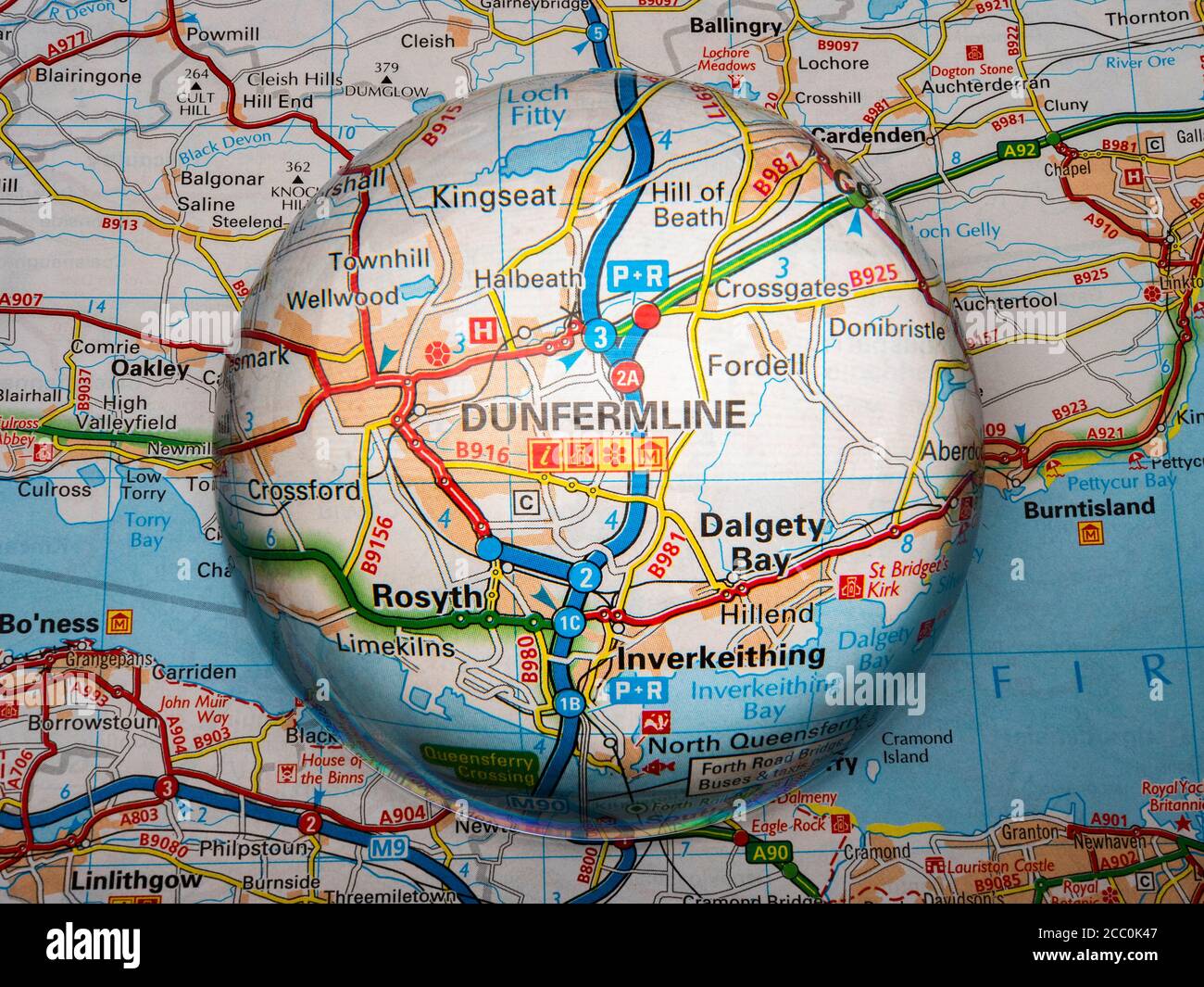 Closeup of a dome shaped magnifying glass over a page of a British road atlas map, with the Dunfermline area of Scotland enlarged for a closer view. Stock Photo