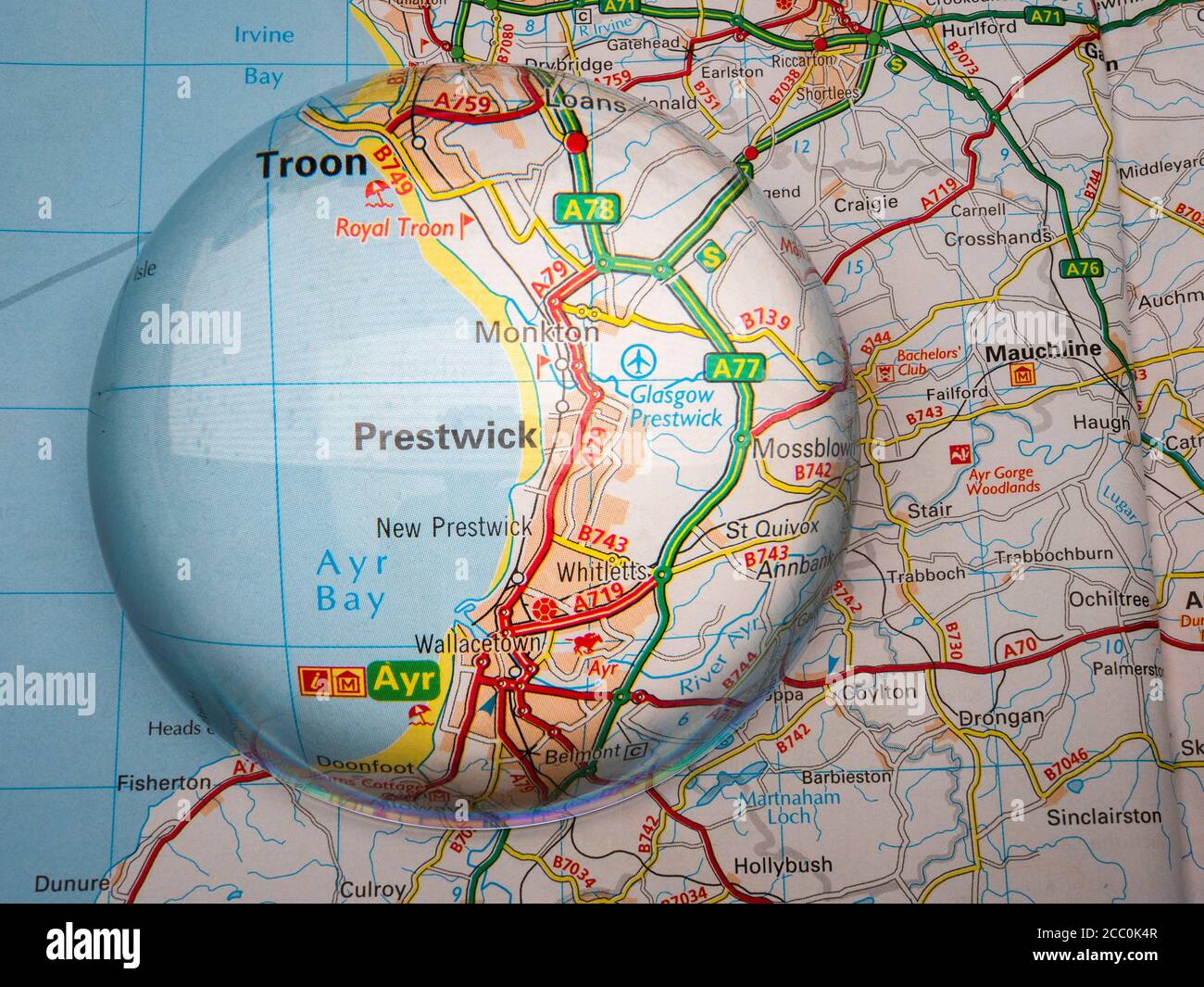 Closeup of a dome shaped magnifying glass over a page of a British road atlas map, with the Prestwick area of Scotland enlarged for a closer view. Stock Photo