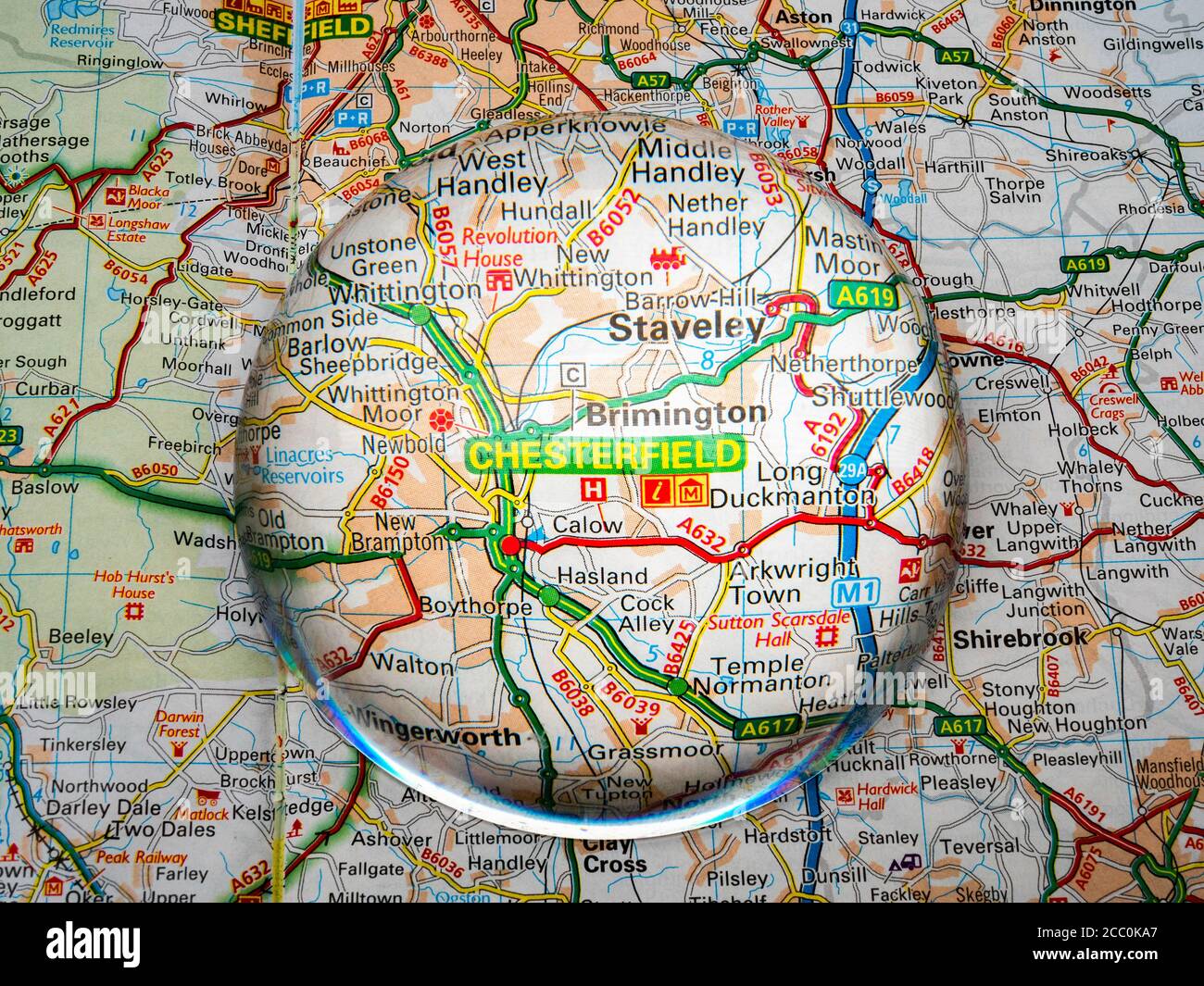 Closeup of a dome shaped magnifying glass over a page of a British road atlas map, with the Chesterfield area of England enlarged for a closer view. Stock Photo