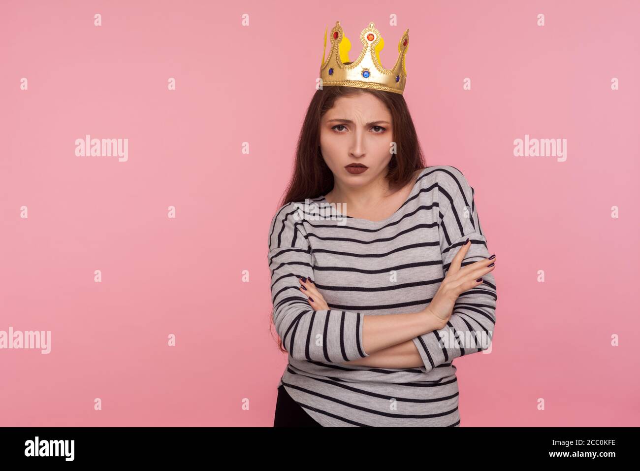 I'm queen! Portrait of egoistic haughty woman with golden crown on head crossing hands and looking with arrogance, her look expressing confidence, sup Stock Photo