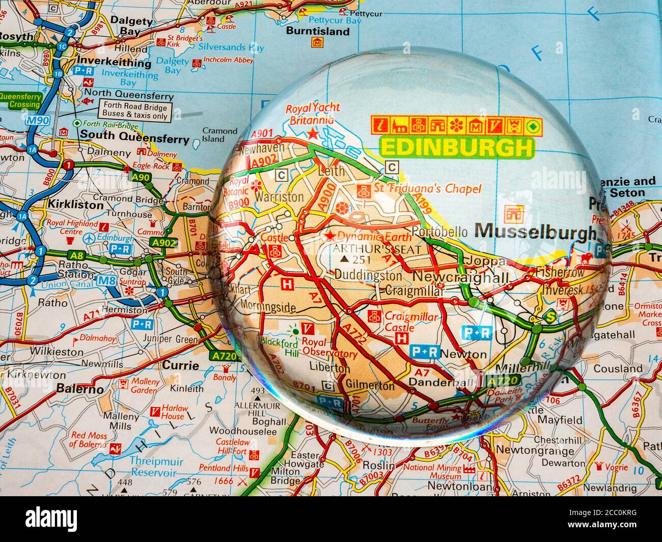 Closeup of a dome shaped magnifying glass over a page of a British road atlas map, with the Edinburgh area of Scotland enlarged for a closer view. Stock Photo