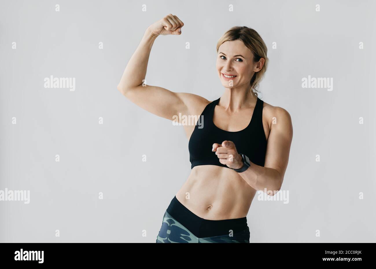 Motivation to workout. Happy woman in sportswear with smart watch demonstrates biceps and muscular body Stock Photo
