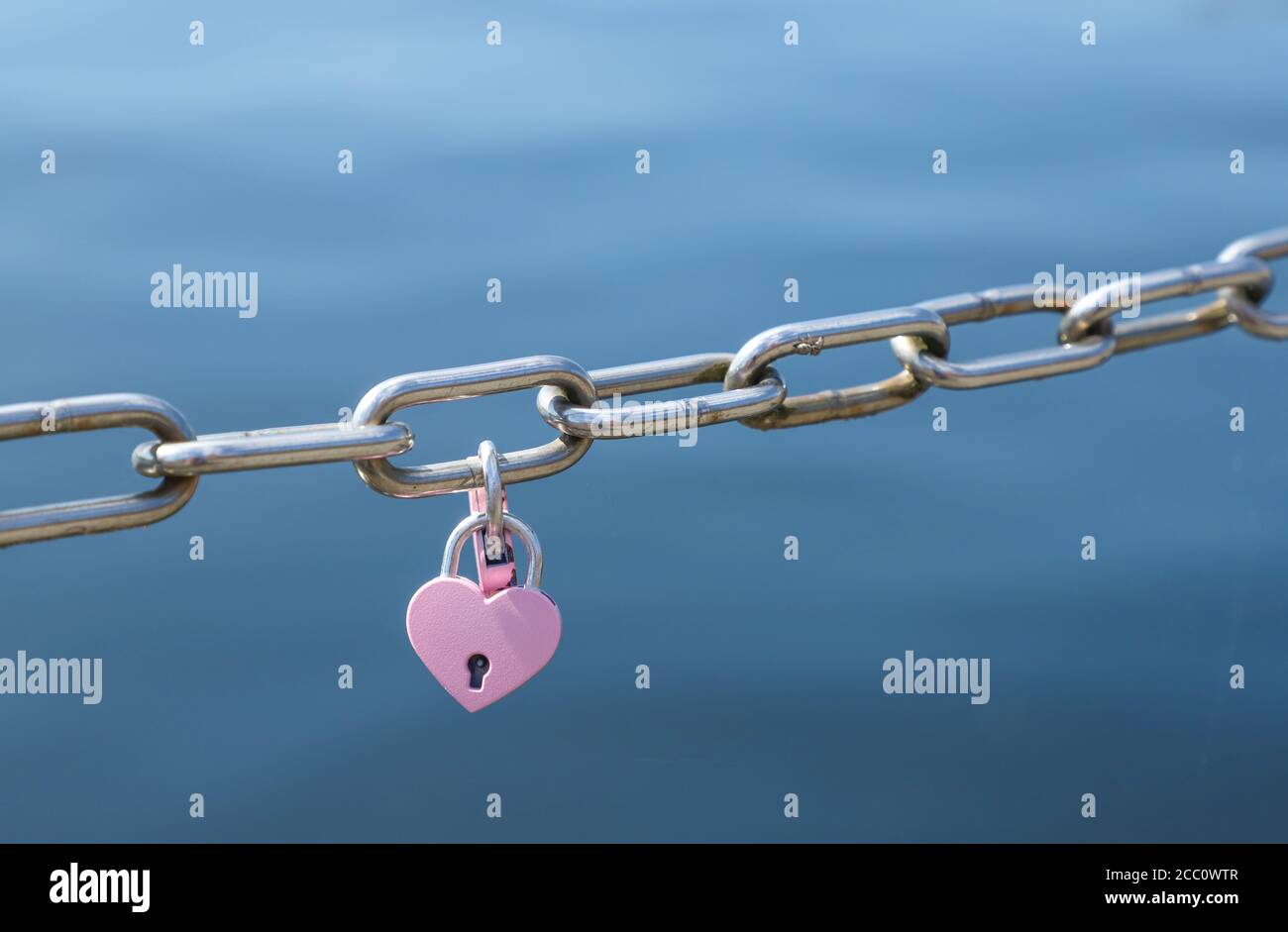 Love padlocks in pink hanging on metal chain fence Stock Photo