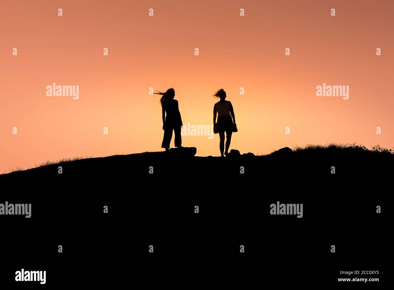 Two women walking on Pentire Point East silhouetted by an intense colourful sunset in Newquay in Cornwall. Stock Photo