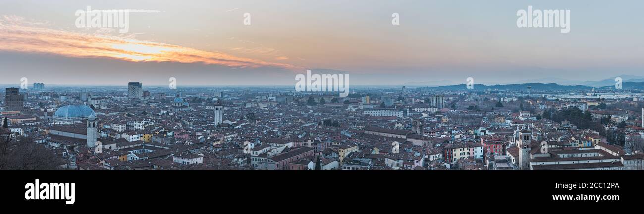 City 's skyline stretching underneath Colle Cidneo at sunset highlights housing space problem, human growth and overpopulation issue - Brescia, Italy Stock Photo