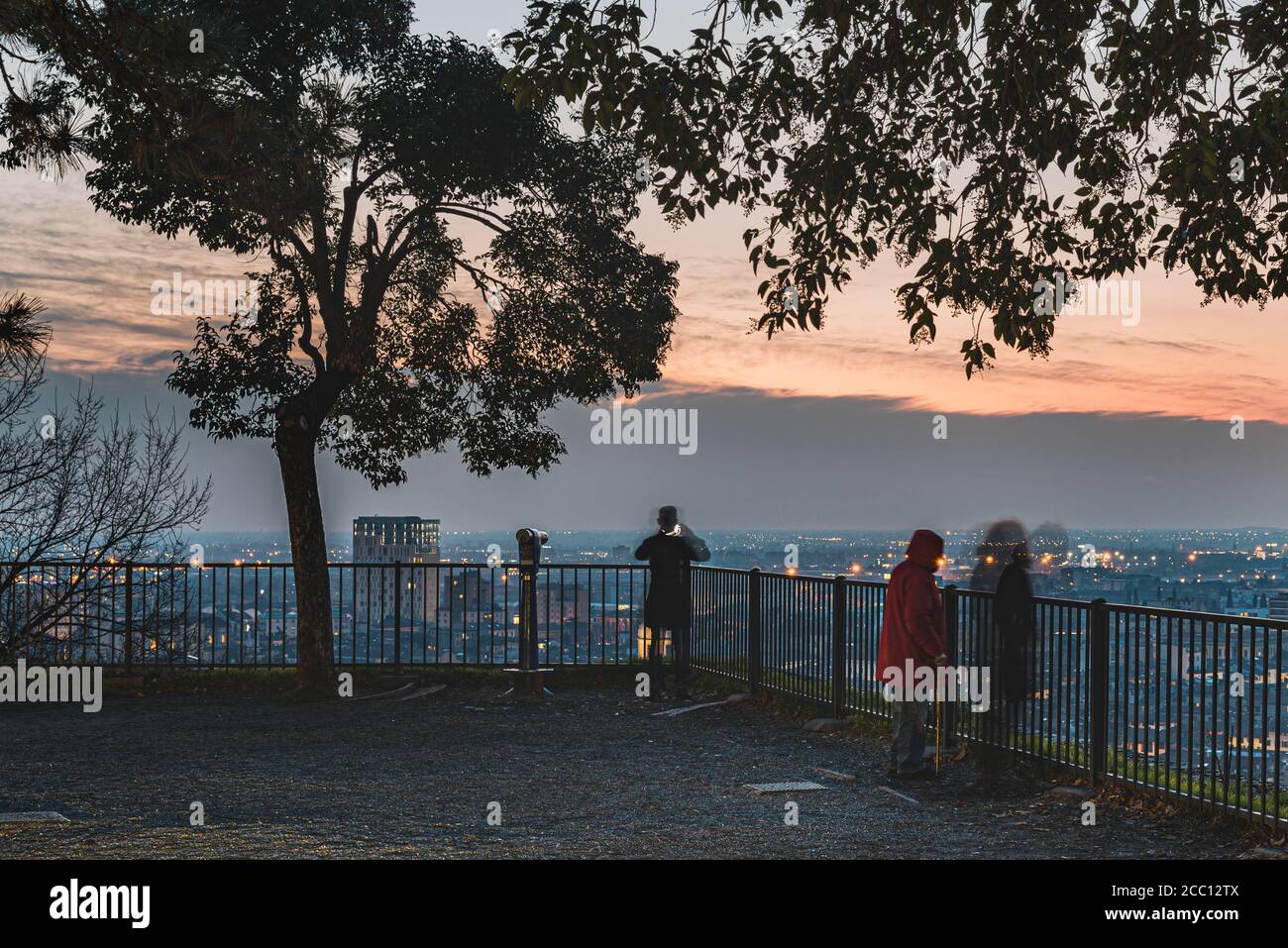 Blurred like people enjoy the city 's skyline from a popular balcony on Colle Cidneo on Piazza del Castello at sunset. Melancholic atmosphere, Brescia Stock Photo