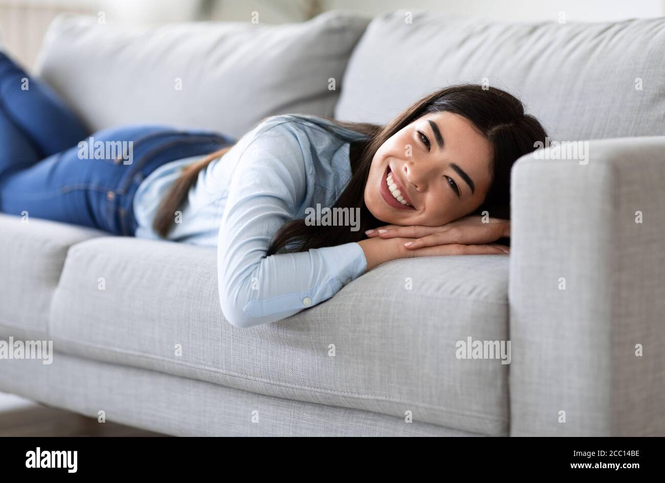 Home Cosiness. Relaxed Asian Girl Lying On Comfortable Sofa In Living Room Stock Photo