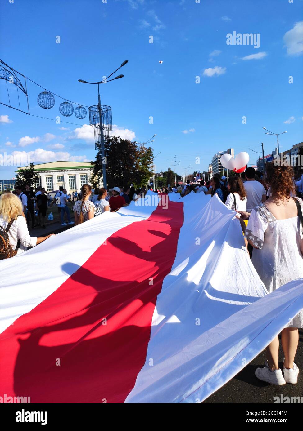 Minsk / Belarus - August 16 2020: Girl demonstrators in white carrying a huge white-red-white flag on the roadway in the capital center Stock Photo