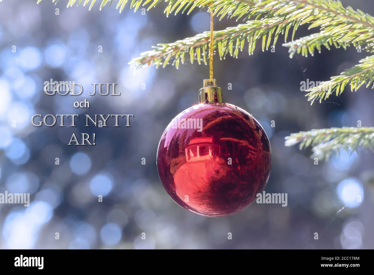 God Jul och Gott Nytt Ar means Merry Christmas and Happy New Year in Swedish, Danish and Norwegian. Red Christmas ball hanging on Christmas tree. Stock Photo