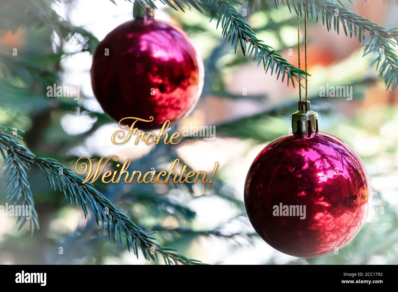 german words frohe weihnachten, which means merry christmas, red Christmas balls with reflection decorate the green branches of the Christmas tree. Stock Photo