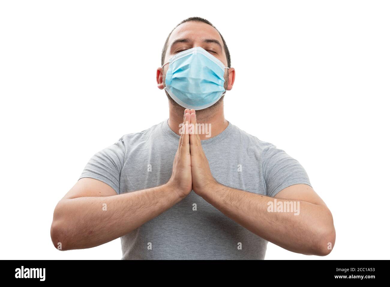 Faithful adult man making praying gesture using hands with eyes closed wearing covid19 pandemic protection disposable mask isolated on white backgroun Stock Photo