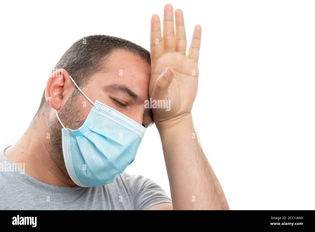 Tired man model wearing medical or surgical disposable mask as covid19 virus infection pandemic protection concept touching forehead with palm fever f Stock Photo