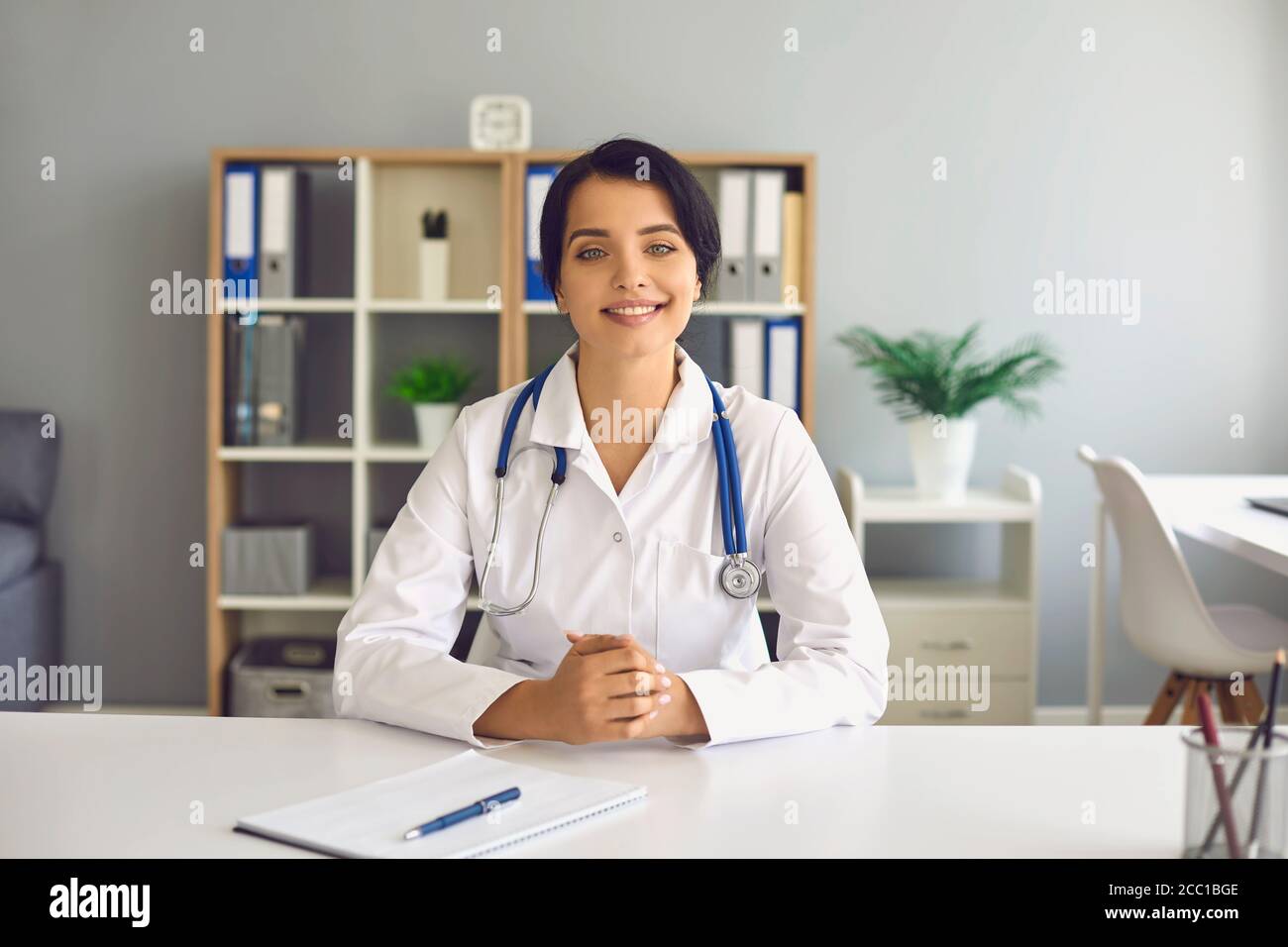 A medical doctor woman in a white coat looks into the camera of a ...