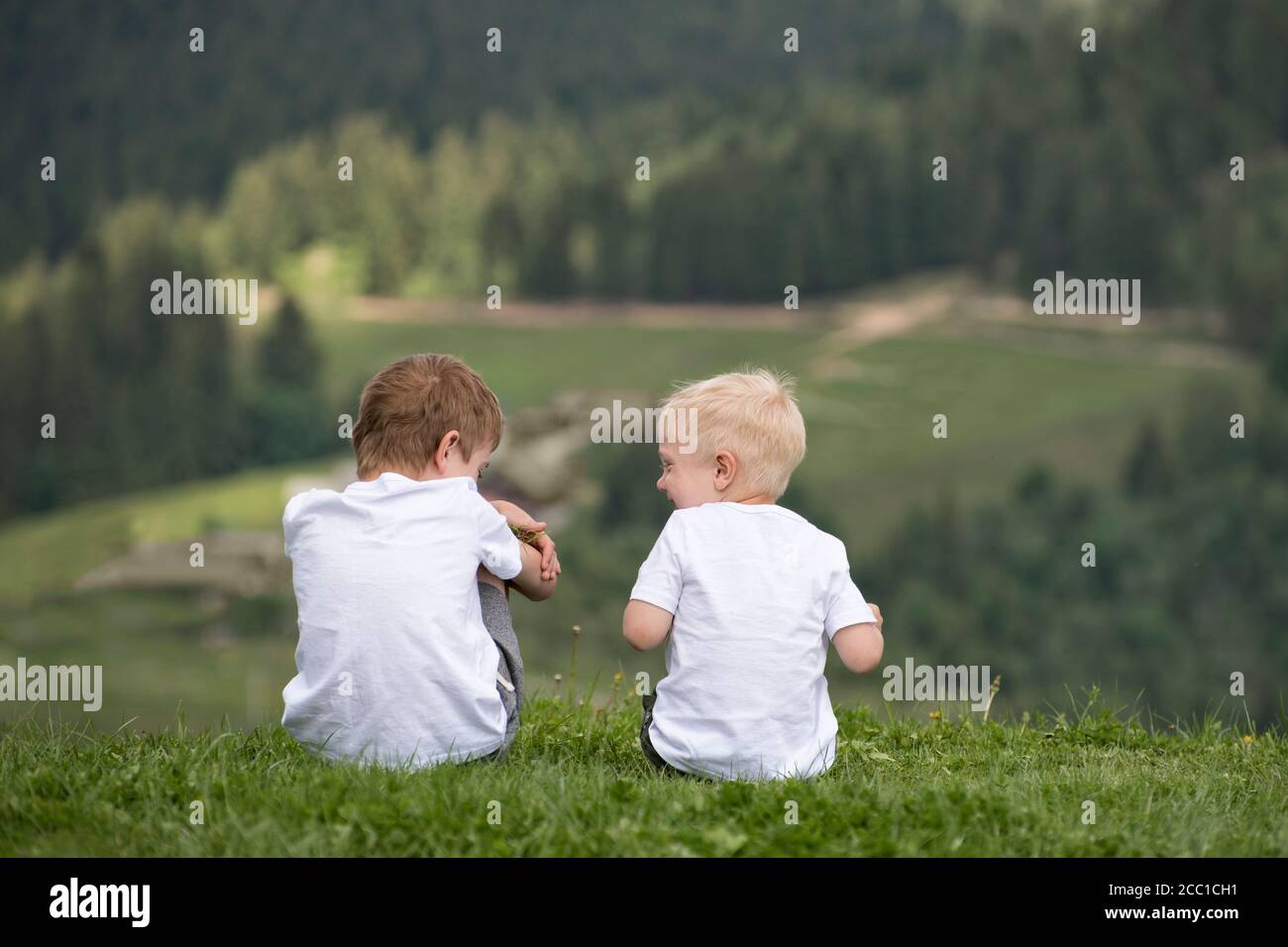 Two boys sit on a hill and have fun. Back view Stock Photo - Alamy