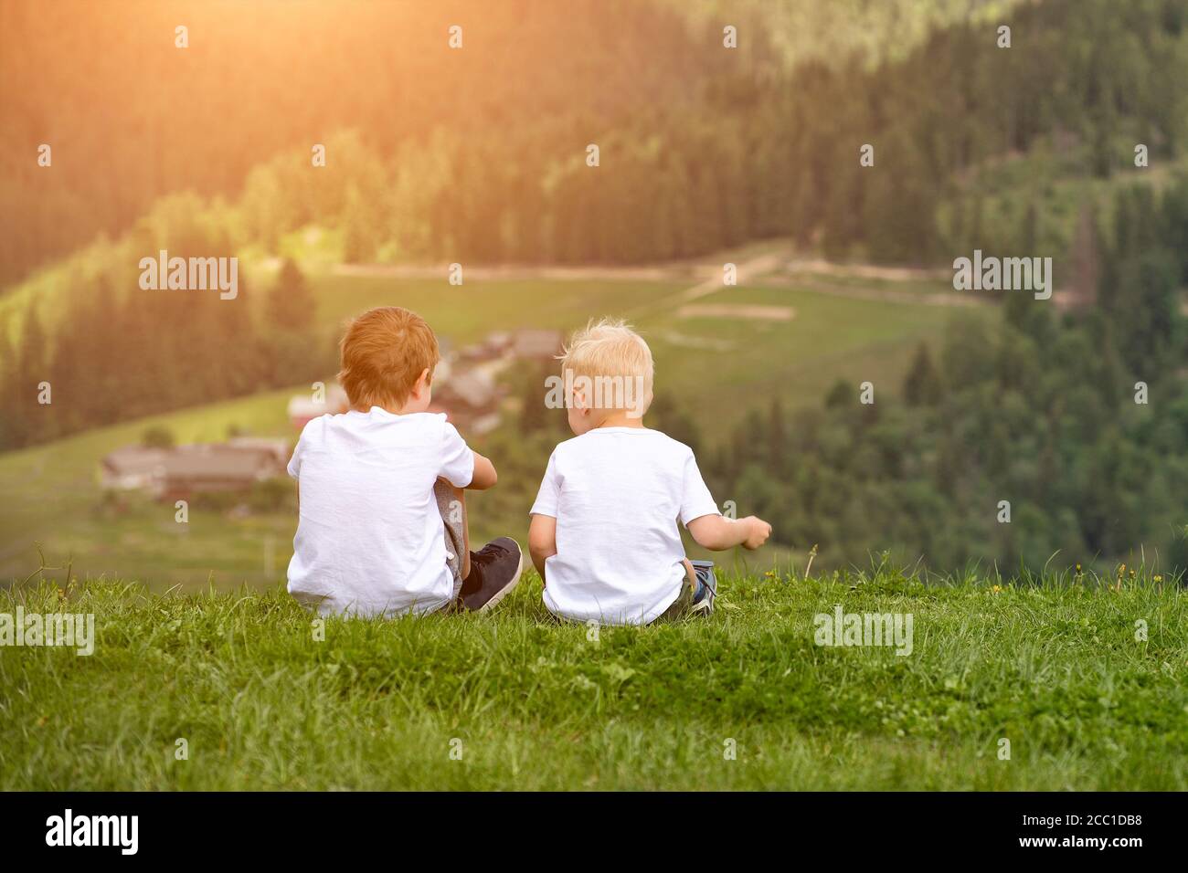 Two boys sit on the hill and talking cheerfully. Back view Stock Photo ...