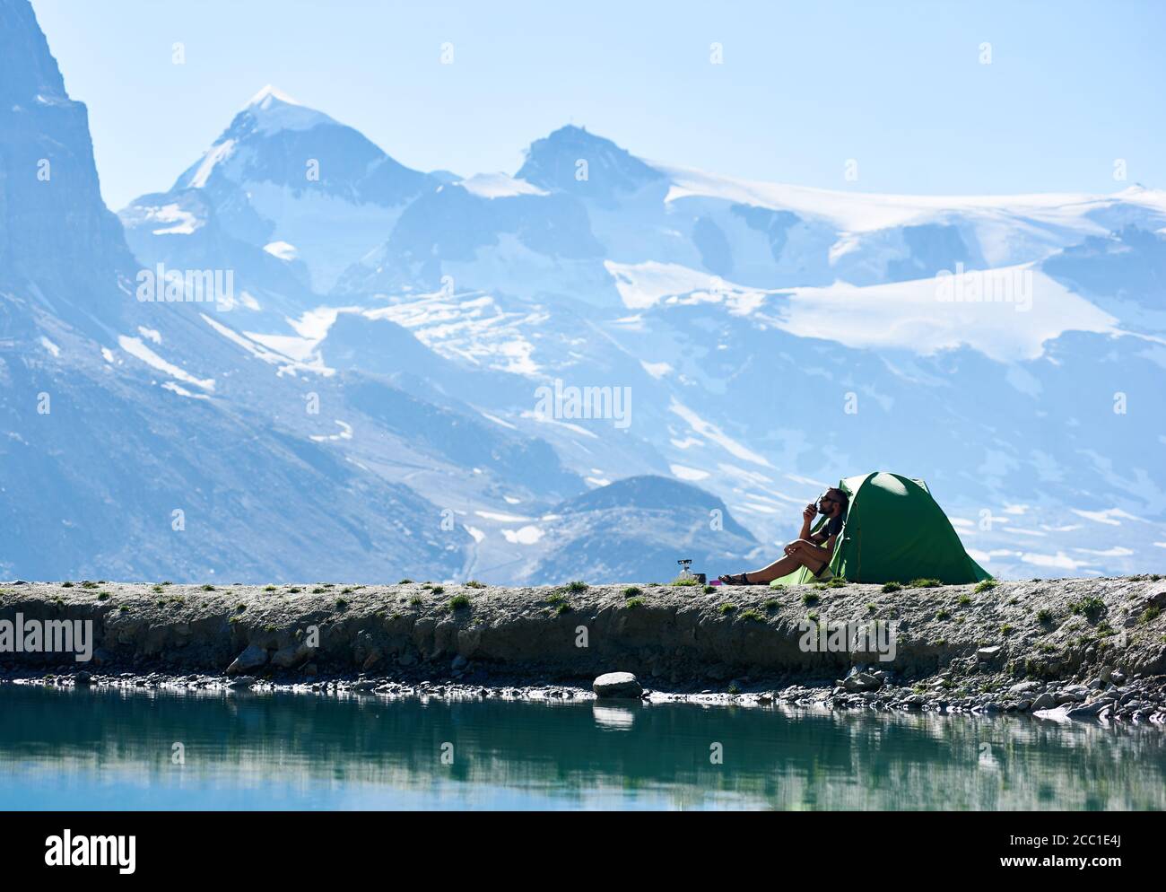 Man enjoying scenery, sitting inside tent in rocky alpine mountains near lake with fresh clear water. Alpinist using radio, talking with friends alpinists in the mountains. Concept of nature beauty. Stock Photo