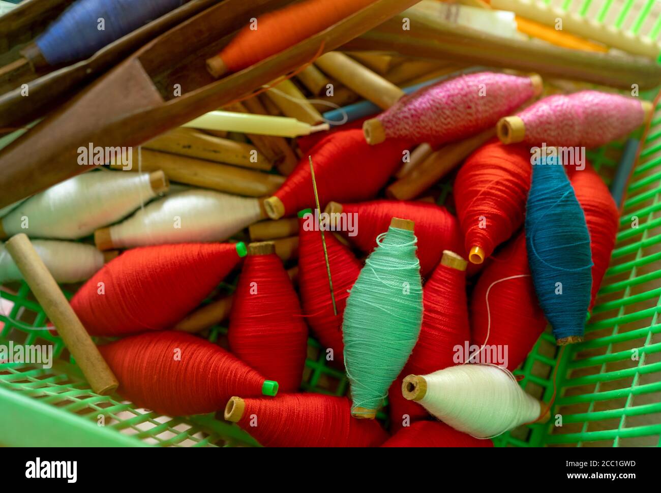 Top view colorful yarns on spool and empty wooden spools in plastic basket. Yarns in weaving shuttle tool. Textile fabric weave tools. Equipment Stock Photo