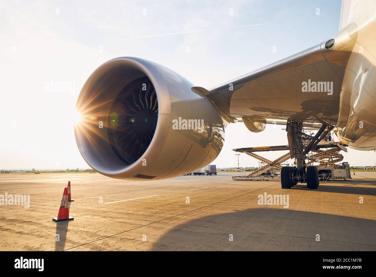 Busy airport at sunset. Large jet engine against loading of cargo containers to airplane. Stock Photo