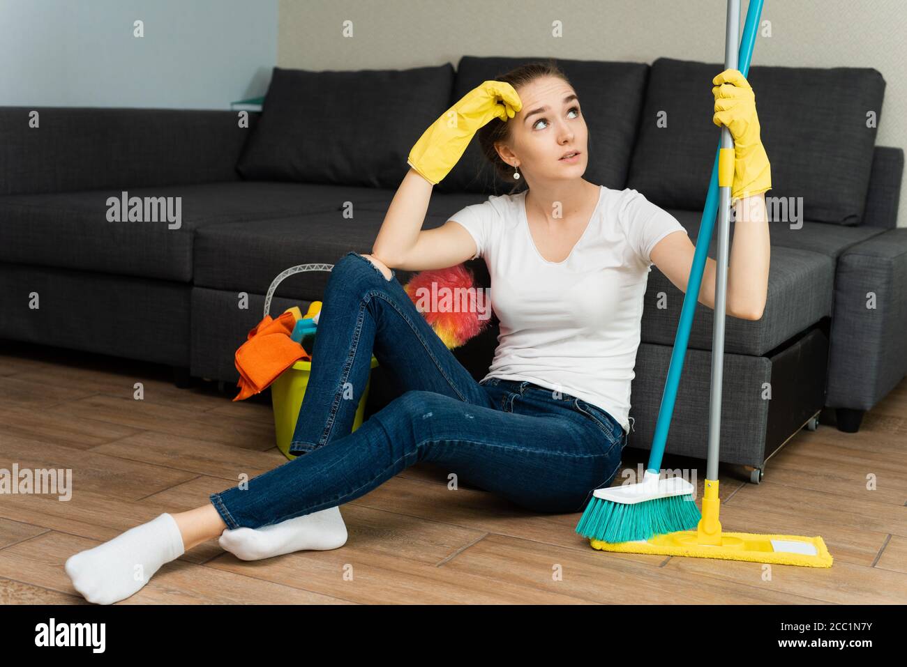 A beautiful woman in rubber gloves next to a coat and cleaning products gets angry at a lot of household chores. Problems of distribution of household duties. Stock Photo