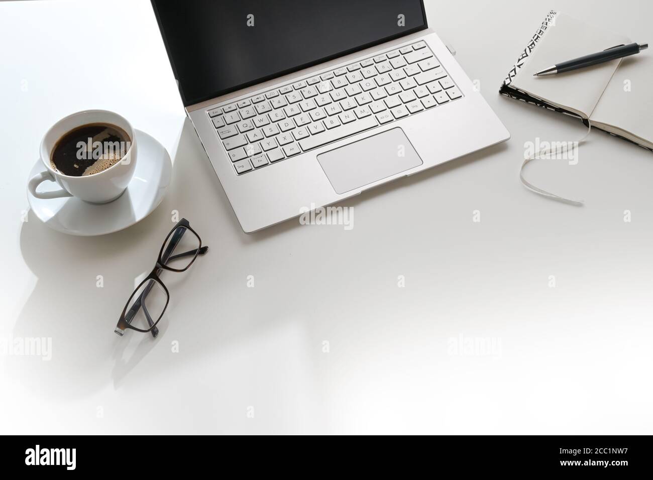 White office desk in sunlight from the back with laptop, notepad and a coffee cup, workplace in a modern company or at home, copy space, selected focu Stock Photo
