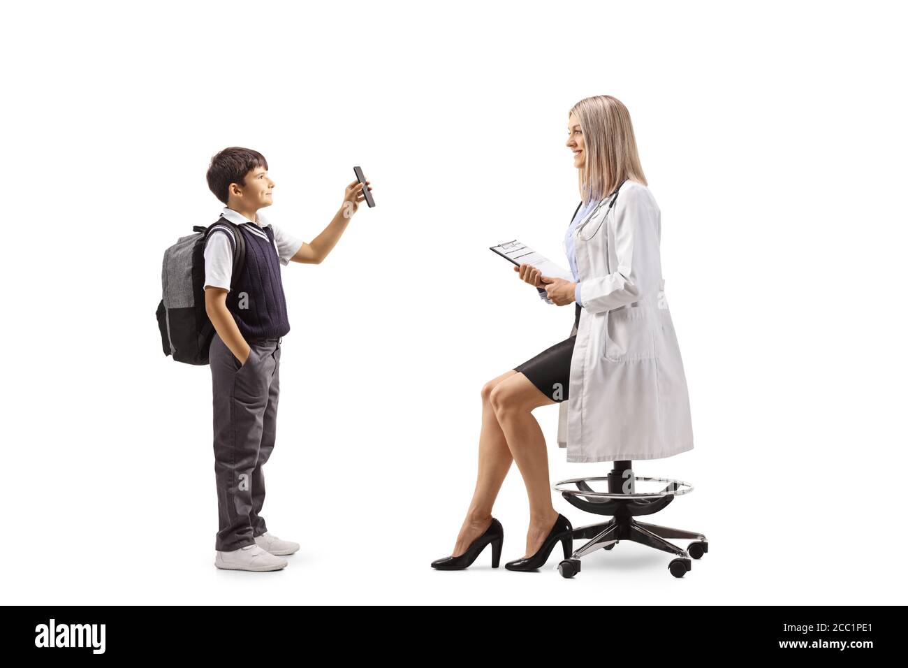 Full length profile shot of a schoolboy standing and showing a mobile phone to a female pediatrician doctor isolated on white background Stock Photo