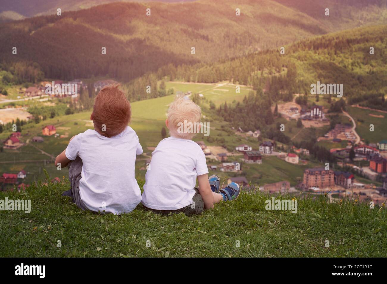 Two boys sitting on a hill and looking at the mountains. Back view ...