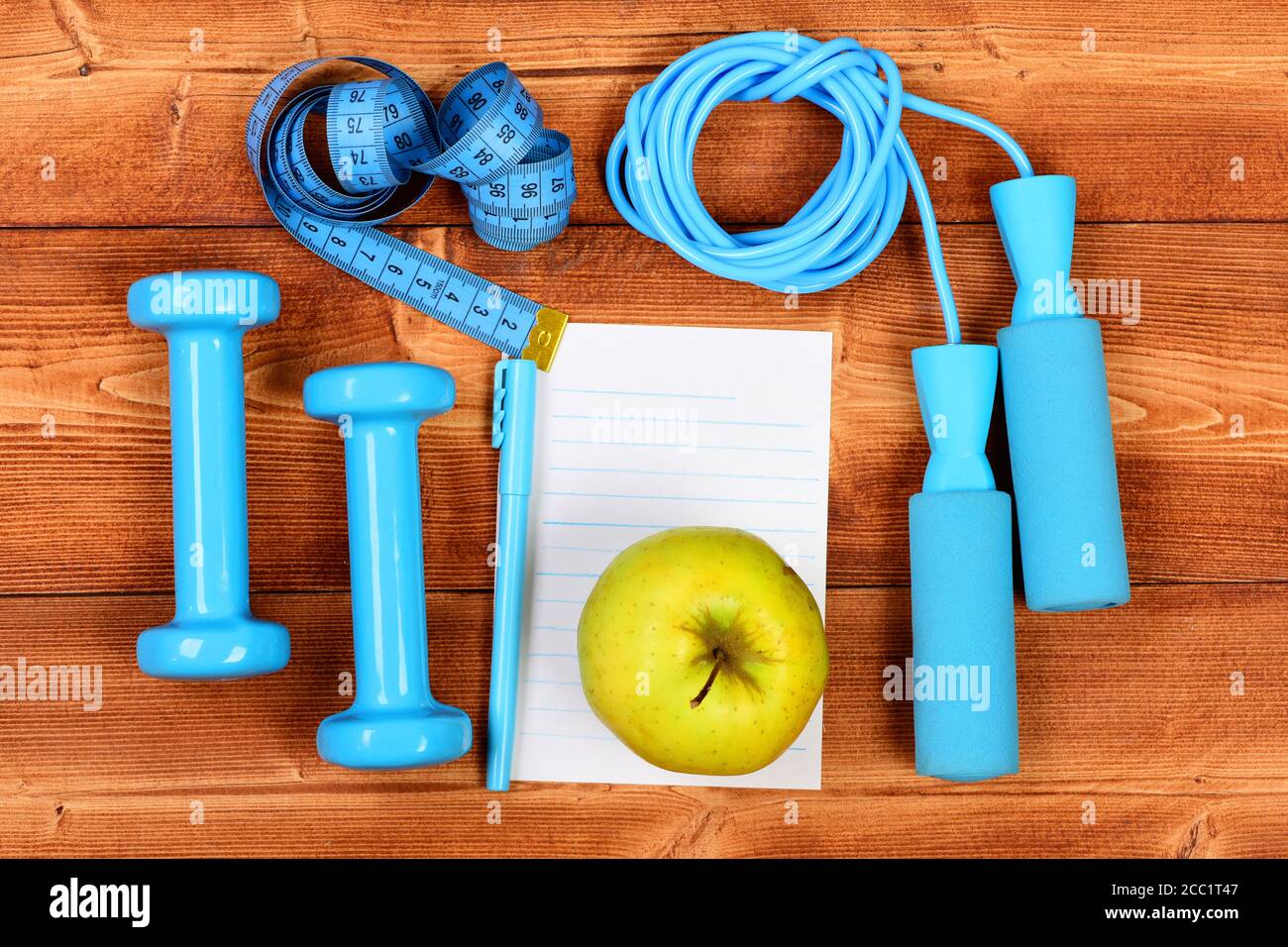 Dumbbells, jump rope, centimeter for weight loss. Fitness tools, blocknote,  pen and apple on brown wooden background. Gym and healthy lifestyle  concept. Sports equipment in cyan blue color, top view Stock Photo 